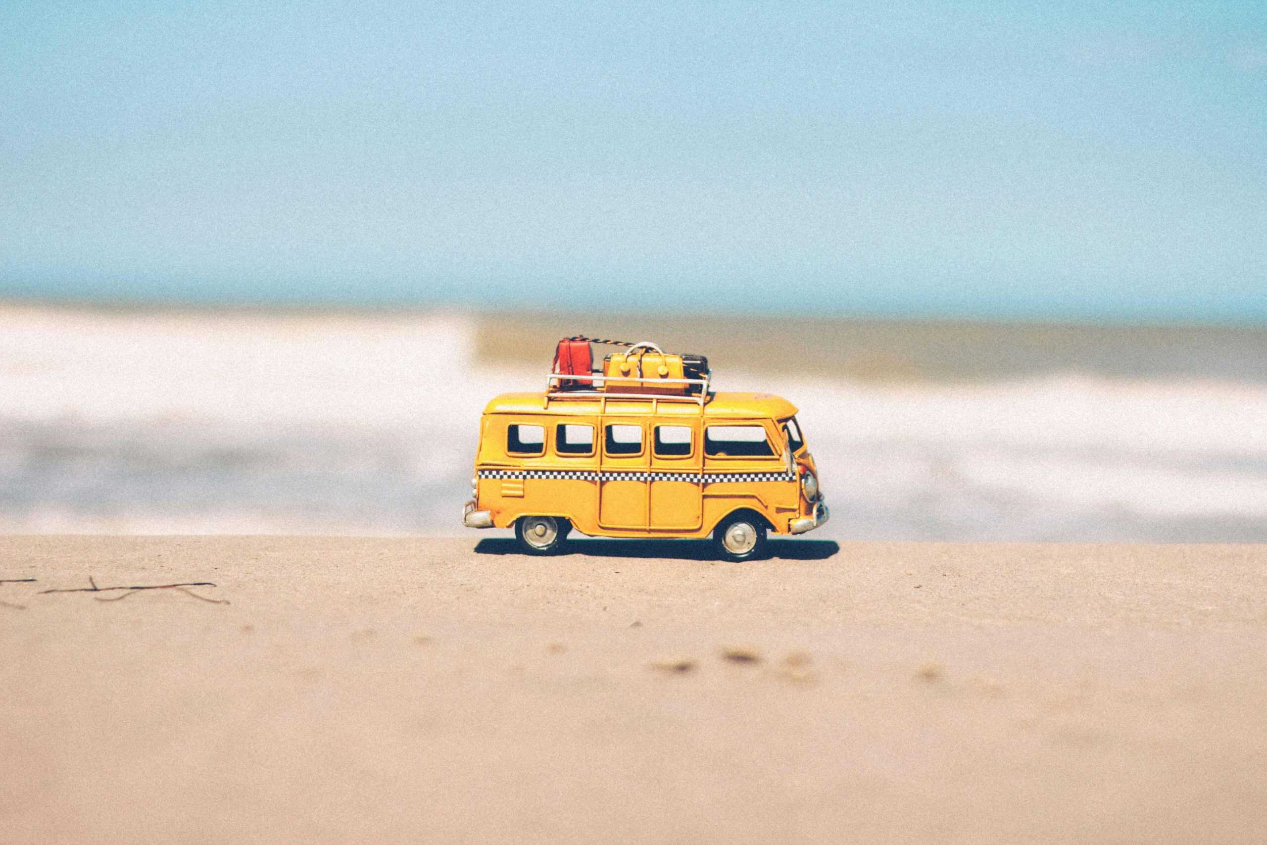Small yellow toy VW van on a beach ready for summer