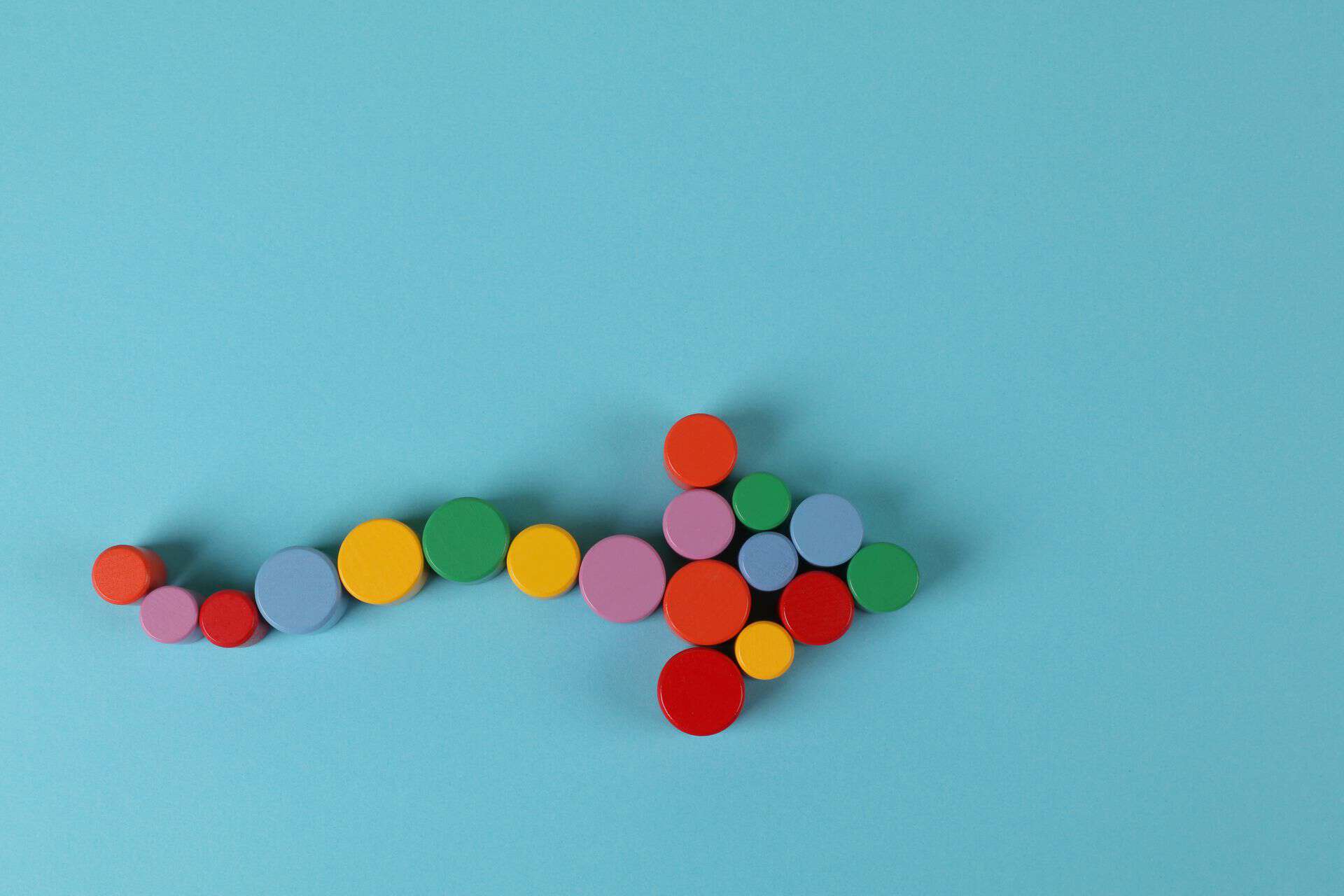 pexels-ann-h-45017-6206451 A vibrant arrow composed of colorful cylinders against a minimalist blue backdrop.