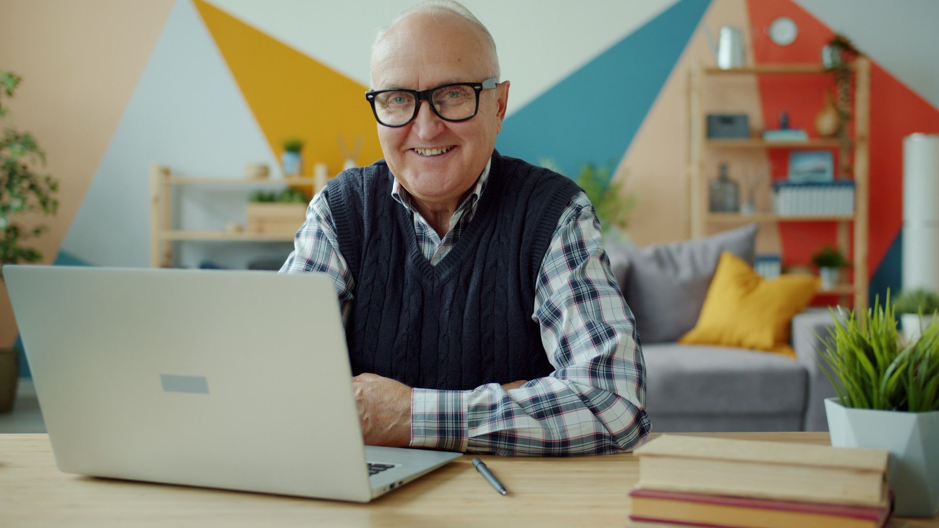 pexels-silverkblack-36764637 Senior man in casual attire smiling while using a laptop in a modern home office setting